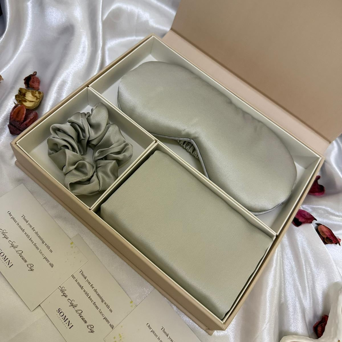 Set of eye mask, scrunchie, and small pouch in a beige box on a white satin background.