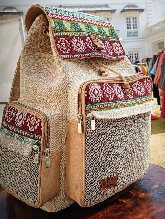 Beige backpack with colorful patterned accents on a blurred indoor background