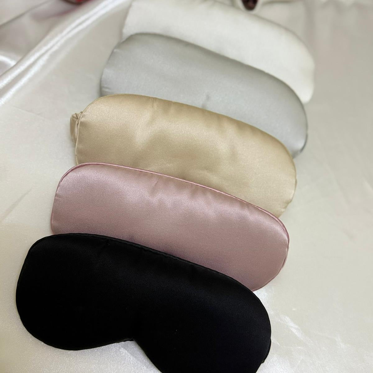 Set of four silk eye masks in different colors on a white surface.