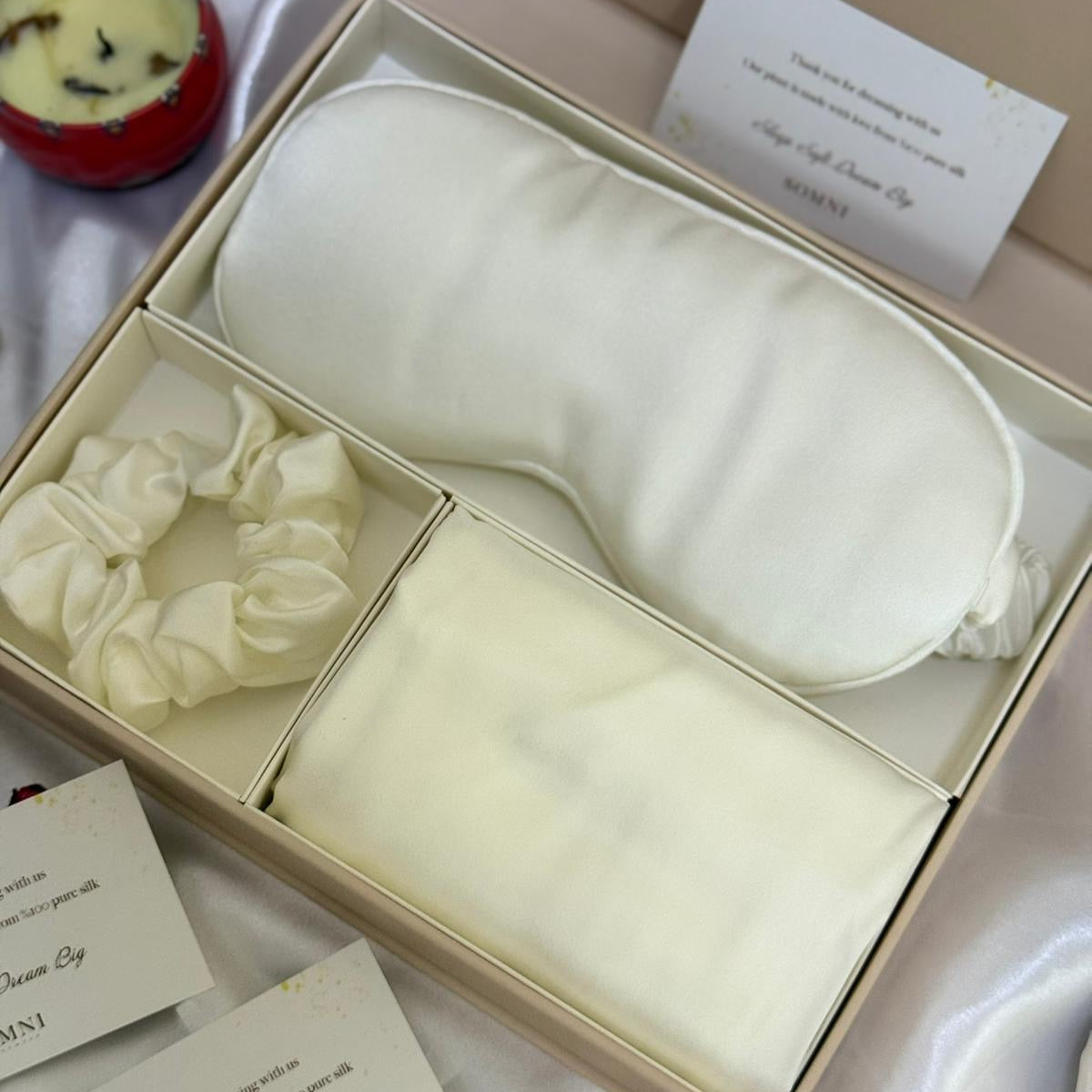 Set of cream-colored sleep mask, hair tie, and pouch in a box with 'SOMNI' branding.